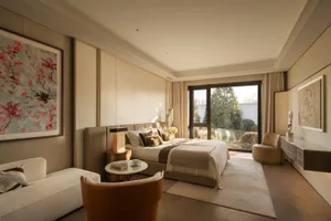 Cozy bedroom with a bed, chair, and couch, surrounded by a beige color scheme, with natural light and wood and fabric materials