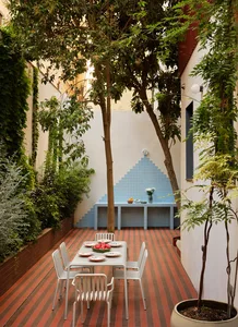 A patio dining area with a table set for a meal, surrounded by chairs and a bench, decorated with potted plants