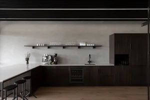 Modern kitchen with wooden cabinets, a black refrigerator, and dim lighting, featuring a sink, microwave, coffee maker, and decorative items