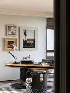 A cozy home office with a wooden desk, chair, and natural light from a window, featuring a lamp and several books on the desk