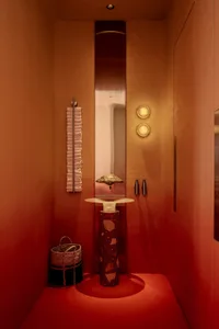 Bathroom with a red accent wall, a white sink on a red table, and two bottles, set in a well-lit space with a warm atmosphere
