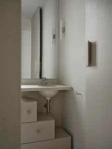 A well-lit bathroom with a white sink, mirror, and toilet, giving a clean and minimalist appearance