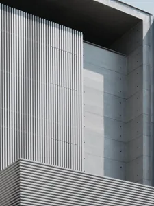 A modern building with a large concrete wall featuring a row of vertical stripes, set against a bright and sunny day