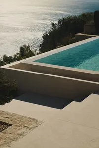 A large pool area with a blue pool surrounded by white walls and flooring, set on a hillside with a picturesque view of the surrounding landscape