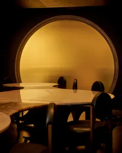 A dimly lit modern dining room with a round wooden table and black chairs, creating a cozy atmosphere