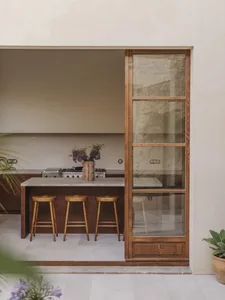 A kitchen with a doorway to a patio, featuring a wooden counter, sink, stools, and a potted plant, with a mix of indoor and outdoor elements creating a cozy atmosphere