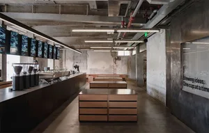 A modern restaurant or commercial space with a cement floor, wooden tables and chairs, and overhead lighting