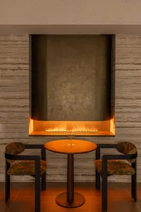Cozy living room with a stone wall, a dining table, and chairs, featuring a fireplace and modern furniture
