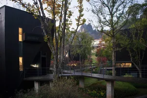 A house surrounded by trees, with a wooden deck and a bridge over a stream, creating a serene and natural atmosphere