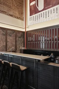 A modern bar with a metal counter, multiple beer taps, and comfortable seating, set in a well-lit atmosphere