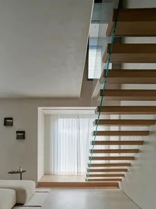 A wooden staircase with a glass railing in a room with a window, lit by natural light