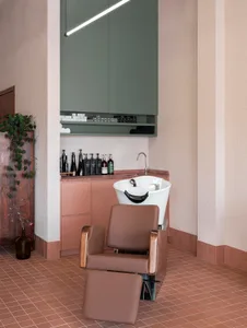A modern hair salon with a pink color scheme, featuring a white sink and a brown chair in a well-lit space with natural light from a window
