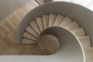 A spiral staircase in a room with a white floor and natural light, surrounded by a calm and inviting atmosphere