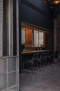 A modern bar with a black counter, wine glass, and bottles, surrounded by chairs in a well-lit restaurant or bar setting