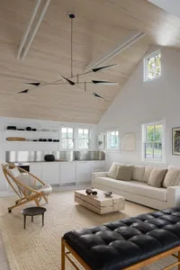 A modern living room with a white couch, chair, and dining table, featuring a kitchen area and natural light from windows