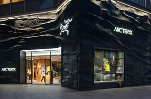 A modern clothing store with a black and white color scheme, featuring a unique rock-like structure in front, surrounded by well-lit interior and customers browsing the merchandise