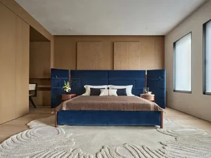 Cozy bedroom with a blue bed, brown blanket, and wooden chair, set against a well-lit background