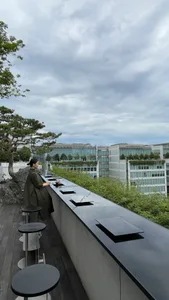 一位女性坐在一座頂樓露台上，周圍是建築物，後景是盆栽和城市景觀