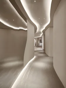 A modern hallway with a curved wall and a lighted walkway, lined with white walls and featuring a concrete floor
