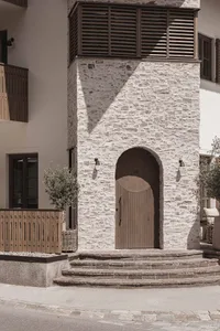 A modern building with a traditional stone archway and wooden door, featuring a brick-like appearance and natural lighting