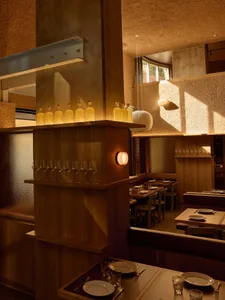 A modern restaurant with a semi-circular seating area, a bar with bottles, and a mix of wood and concrete walls, lit dimly for a cozy atmosphere