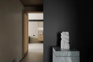 A black and white living room with a stone pedestal, a white sculpture of a hand, a couch, and a dining table, in a modern and minimalist style