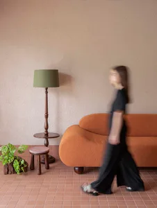 A woman walks towards a couch in a warm and inviting living room with brown furniture and natural lighting