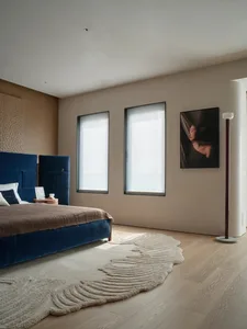 A well-lit bedroom with a bed, chair, and painting, featuring predominantly wooden materials and a comfortable atmosphere