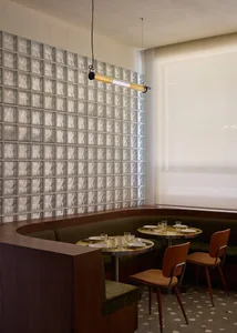 A cozy restaurant interior with a long wooden dining table and chairs, set with cups, bowls, and wine glasses, under warm lighting