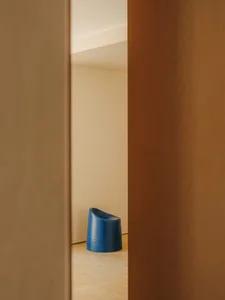 A small, white room with a blue chair near the door and a blue trash can in the center, creating a minimalist and clean atmosphere