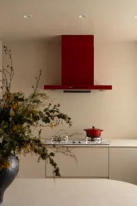 Modern kitchen with a red oven and cabinet, white countertops, and natural light from a window