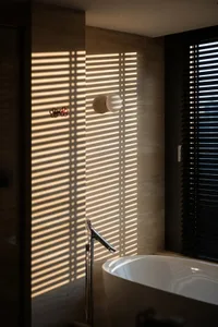 A modern bathroom with a white bathtub, shower head, and tile walls in a dimly lit space