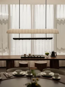 Dining room with a wooden table, chairs, and a potted plant, set with various items and a vase with flowers, in a warm and inviting space with natural lighting