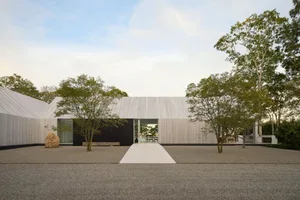 A modern house with a wooden exterior, large window, and door, surrounded by trees in a residential area