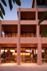 A pink library building with floor-to-ceiling windows, allowing natural light to enter and illuminating books on the windowsills