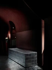 A small, dark room with a metal bench against a red wall, creating a moody and intimate atmosphere