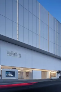 A modern building with a white exterior and a large window, set against a bright and sunny background