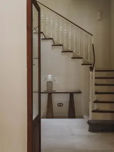 A wooden staircase with a white wall and a glass door, set in a calm and serene atmosphere with natural lighting