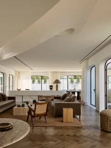 Cozy modern living space with a white color scheme, a large couch, chair, dining table, and potted plants, set in a well-lit room with natural light from windows