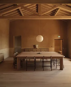 Warm dining space with a wooden table, chairs, and a potted plant, surrounded by wooden floor and inviting atmosphere