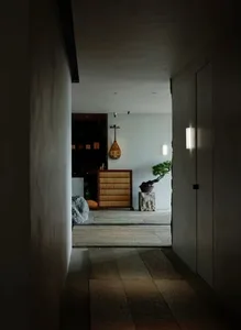 A dimly lit hallway with white walls and a stone floor, featuring a doorway and a potted plant near the end of the hall