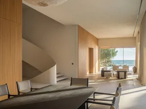 Cozy living room with a dining table, chairs, and a couch arranged around the table, a spiral staircase, and a large window with natural light