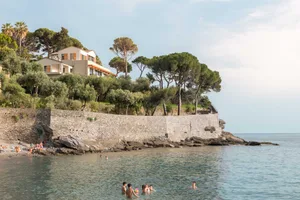 A group of people swim in the ocean, surrounded by a rocky landscape and a blue beach setting, capturing a relaxed and leisurely atmosphere