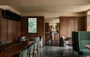 A hotel lobby with a dining table surrounded by chairs, a wooden floor, and a large mirror on the wall, set in a well-lit space with a welcoming atmosphere