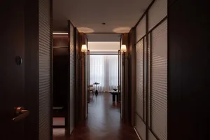 Dimly lit hotel hallway with a wooden floor, a glass door, a couch, a chair, and a vase on a surface