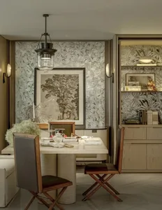 A warm and inviting living room with a dining table, chairs, couch, bookshelf, vase, and potted plant, surrounded by wood and metal materials, illuminated by natural light