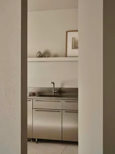 A modern kitchen with a stainless steel sink, white refrigerator, and tile backsplash, featuring two cups on the countertop in a dimly lit space