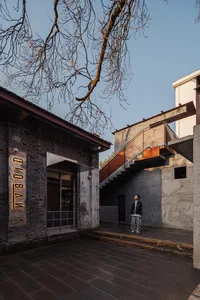 A stone building with a concrete staircase leading to a second floor, set in a quiet outdoor environment with a tree in the background