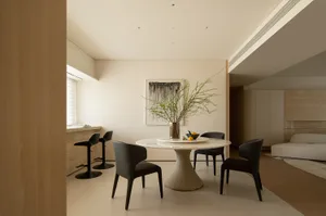 A modern living room with a dining table and chairs, surrounded by comfortable furniture and natural light from the windows