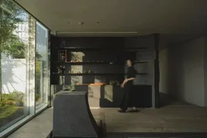 A woman walks towards a counter in a calm and inviting dining area with a black and white color scheme and a window in the background